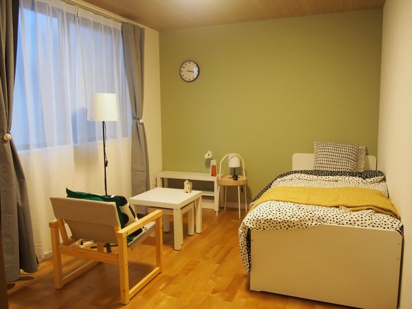 グリーンの壁紙を背景に、落ち着いたカラーの家具と寝具が置かれた部屋。