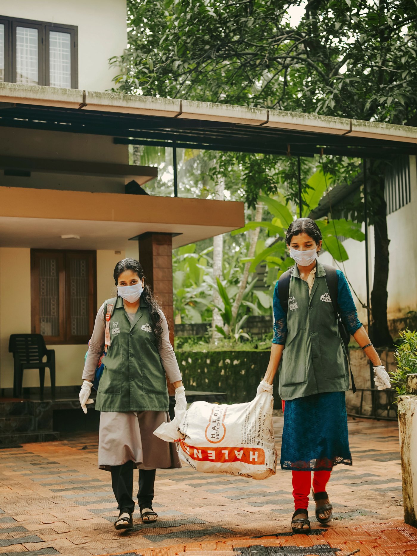 Zwei Personen gehen eine Straße entlang. Sie tragen Taschen, die mit Glasflaschen gefüllt sind.