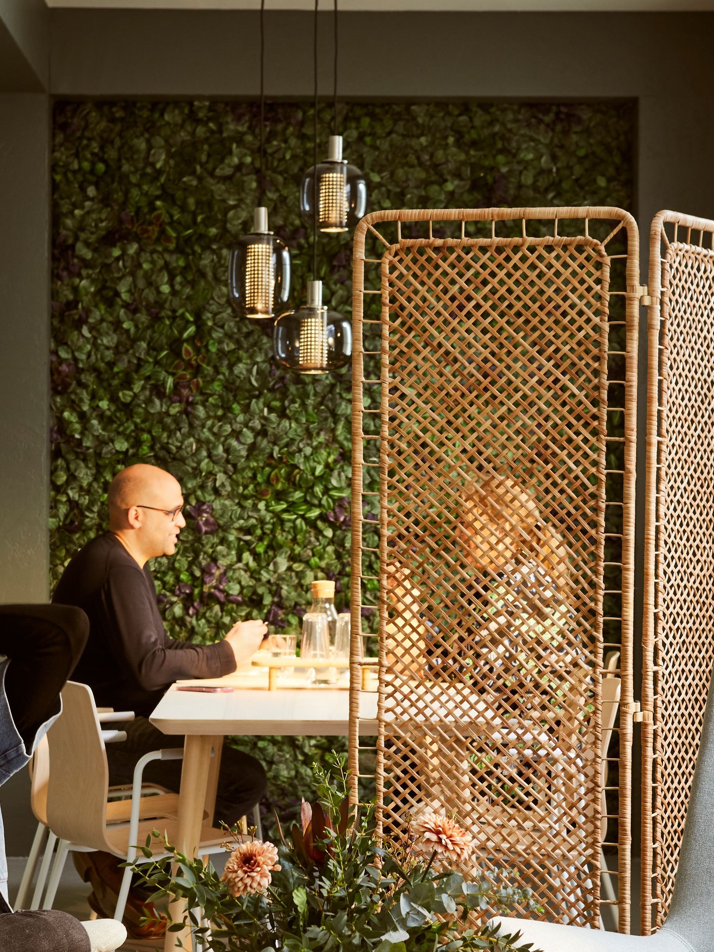 A sunlit interior with light-green VEDBO armchairs around a JAKOBSFORS coffee table. Artificial plants cover the far wall.