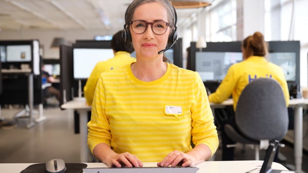 Een IKEA specialist in winkelen op afstand zit aan haar bureau en draagt een headset.