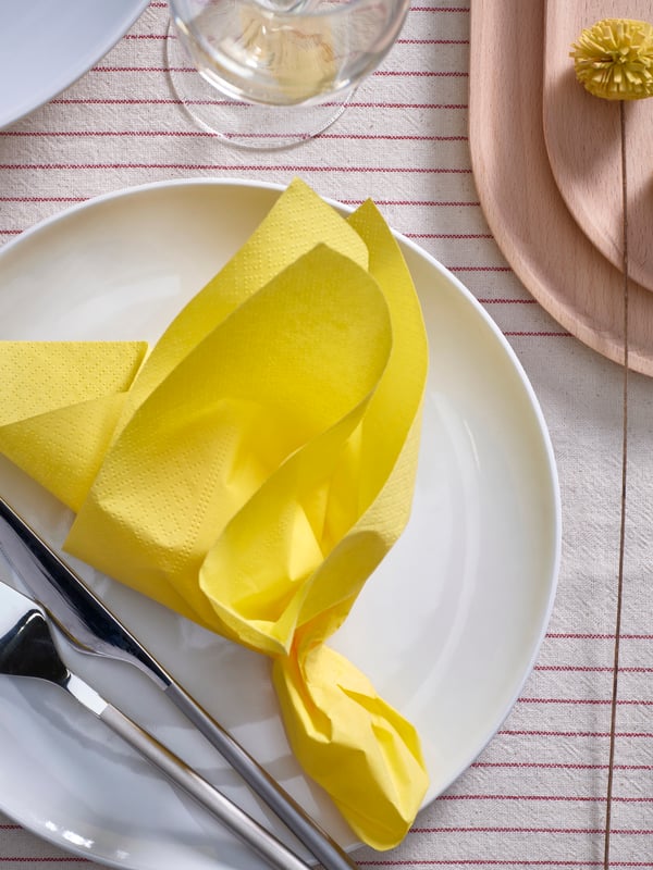 Une serviette en papier jaune pliée sur une assiette blanche 