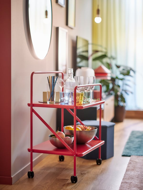 A red JÄRLÅSA side table on castors with BLANDA BLANK serving bowls on it stands under a LINDBYN mirror mounted on a wall.