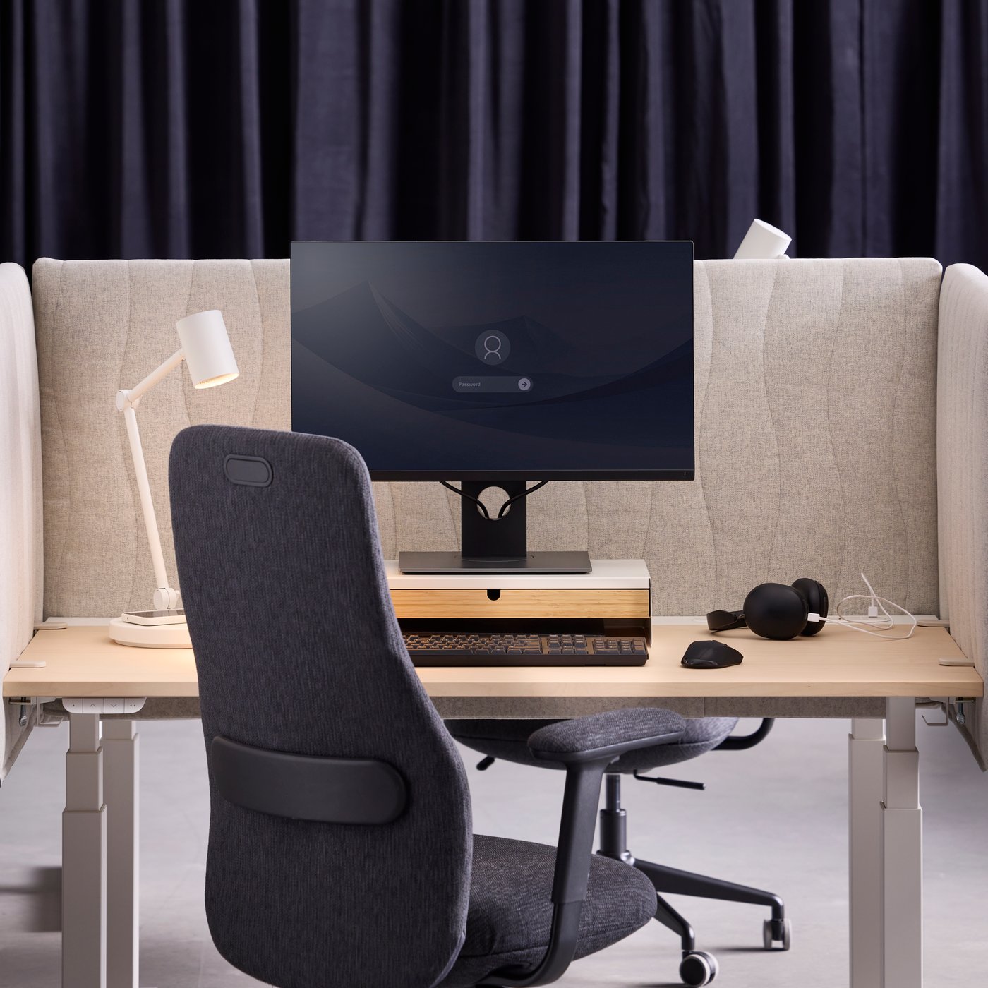 A workspace with a beige MITTZON acoustic screen made from Gunnared fabric separates the desk from the background.