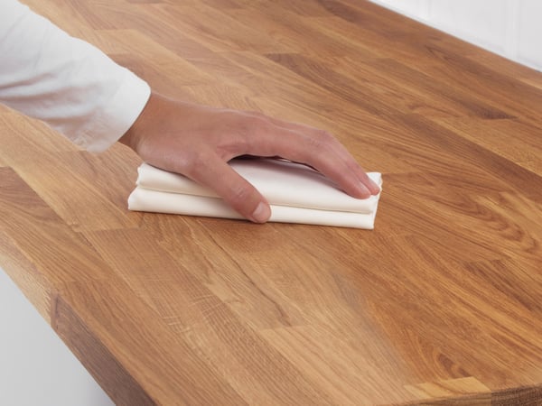 A person’s hand pressing down on a folded piece of paper on a wooden surface.