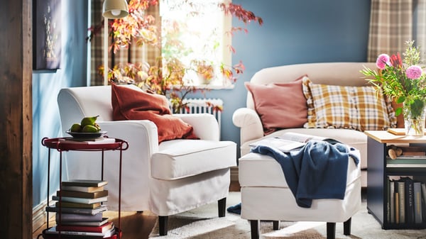 A white ROCKSJÖN armchair and a white ROCKSJÖN footstool stand beside a light beige ESSEBODA sofa in a bright living room.
