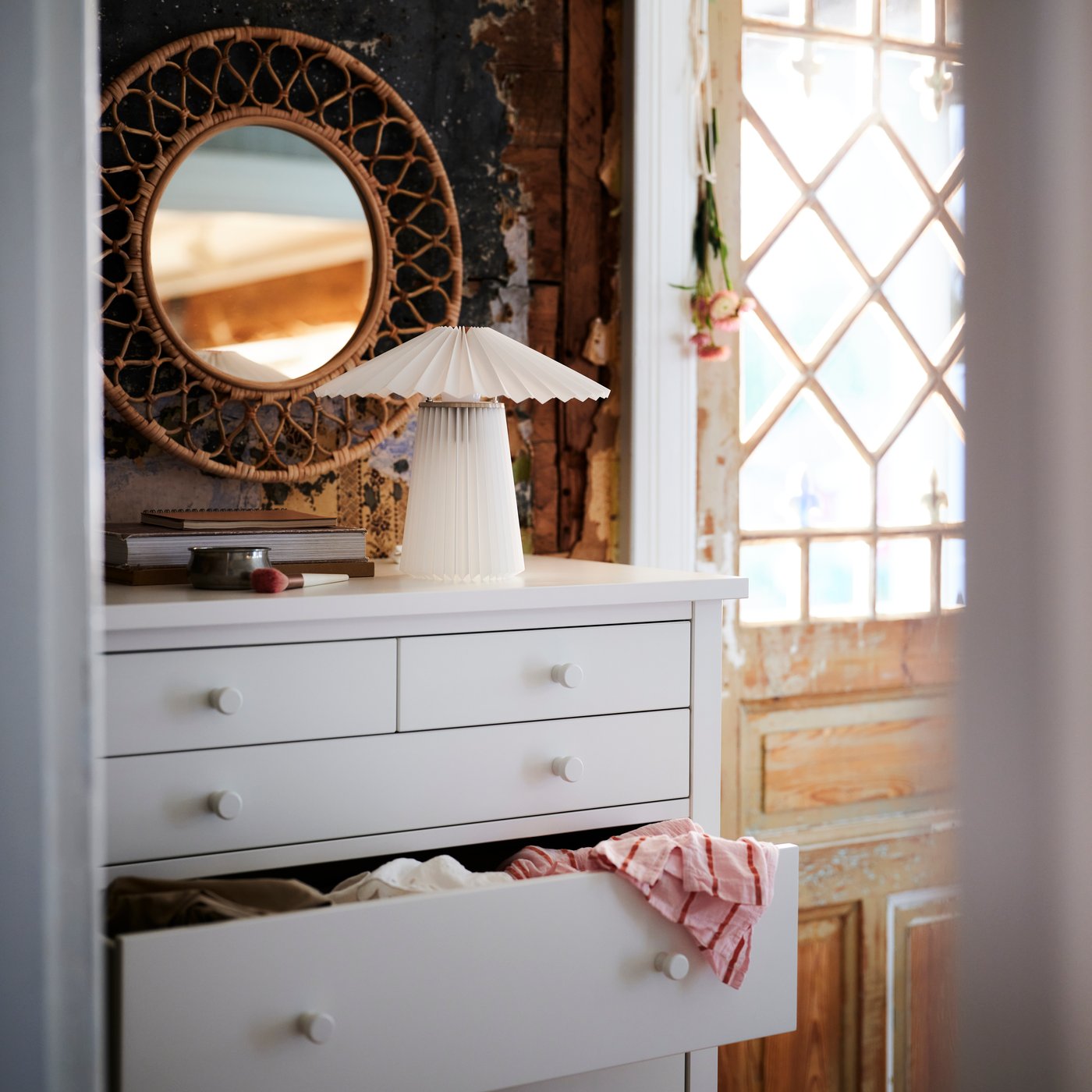 I et rustikt rom står en GULLABERG-kommode med 6 skuffer under et rundt speil med en lampe og små dekorative ting på toppen.