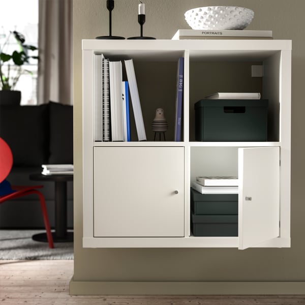 A wall section of a light room with a wall-mounted KALLAX shelving unit fitted with inserts with doors and decoration on top.