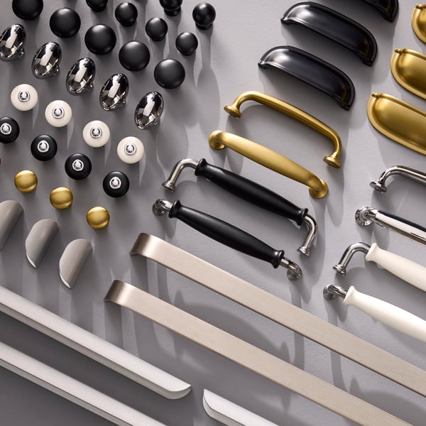 Handles and knobs for kitchen fronts, in different colours and different expressions, are placed in rows on a grey surface.