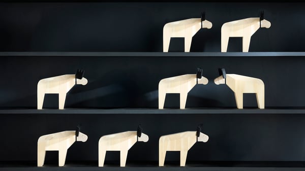 Drei Regalbretter mit insgesamt acht stilisierten Tierfiguren aus hellem Holz, die Elche darstellen. Die Figuren stehen auf schwarzem Hintergrund – drei oben, zwei in der Mitte und drei unten.