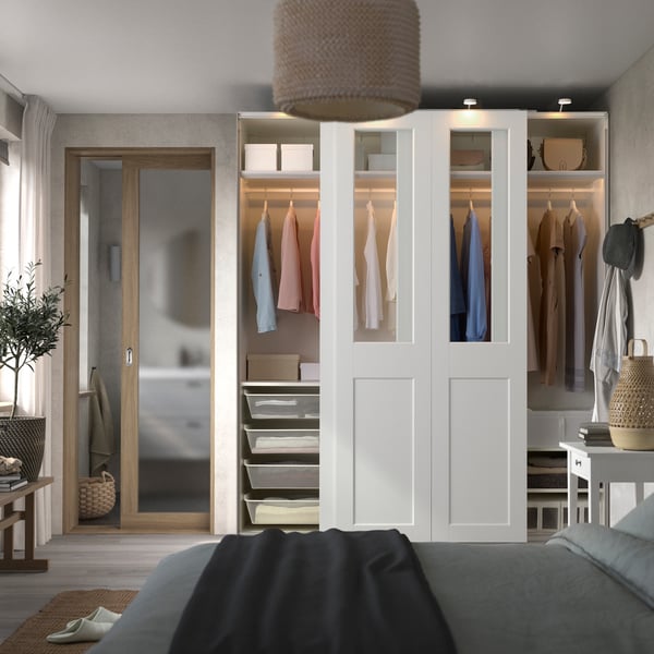 A PAX wardrobe solution is on the side of a bedroom next to the door to the master toilet. The wardrobe has clothes and containers inside of it and has a wooden door with glass panels