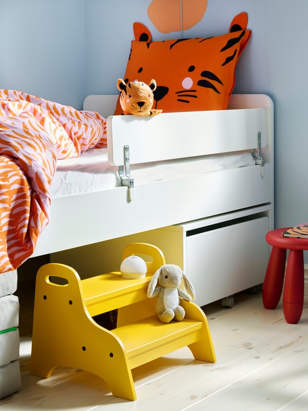 Ein weißes SLÄKT Kinderbett und eine faltbare SLÄKT Matratze unter dem Bett.