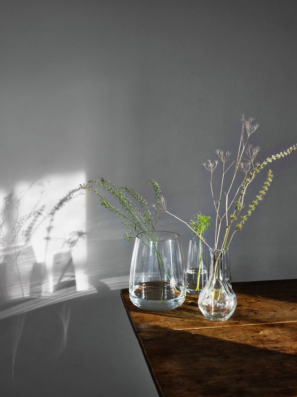 Two clear glass BEGÄRLIG vases hold dried flowers, branches and SNÖYRA LED lighting chain on a festive table.
