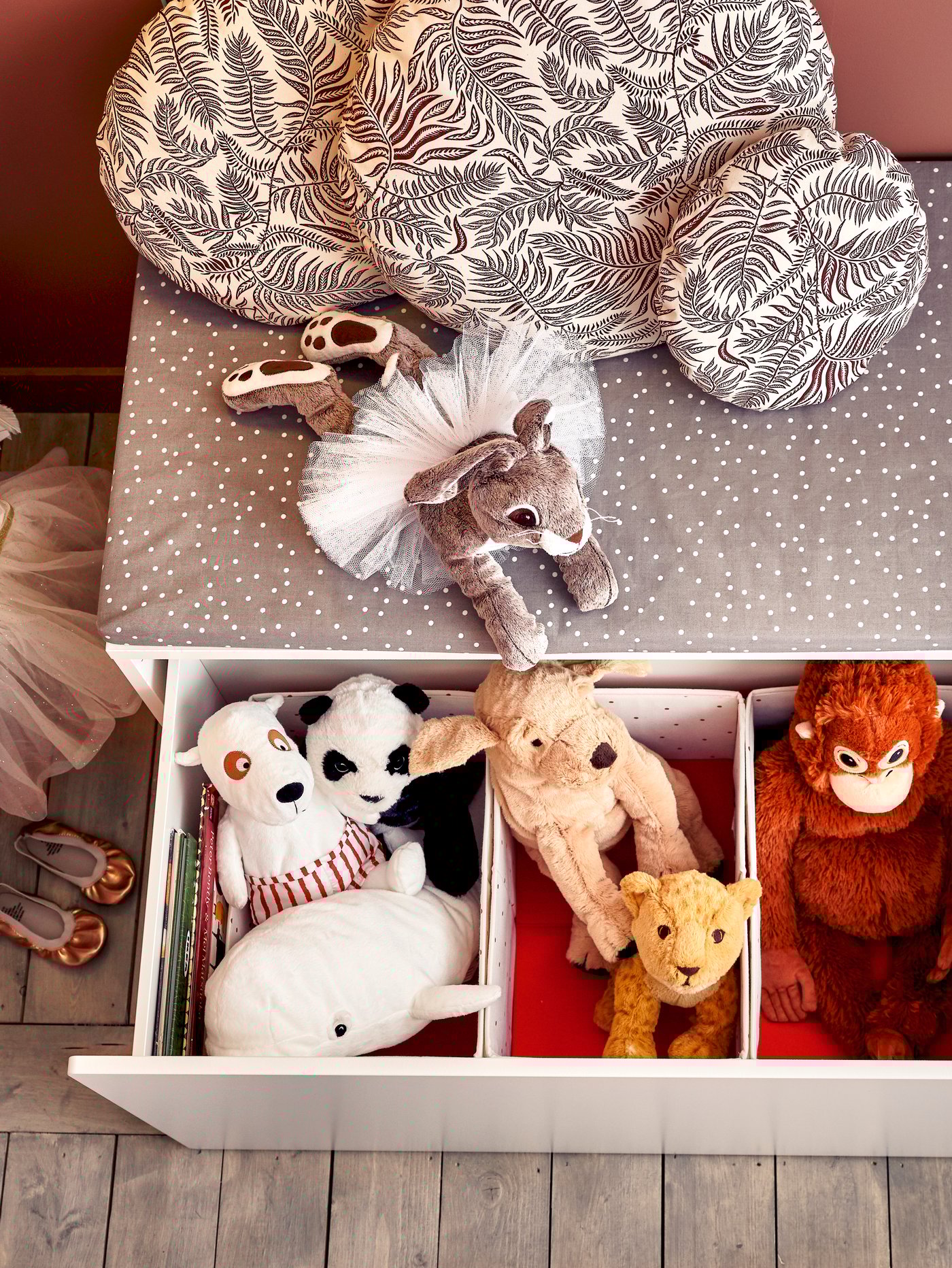 Vista superior de una caja rectangular con un cajón abierto que contiene peluches en cajas. En la caja hay un cojín de banco gris.