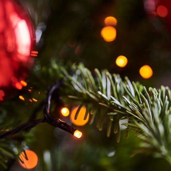 Un primo piano di un albero di Natale addobbato con una palla rossa lucida e luci calde sfocate, che creano un'atmosfera festosa.