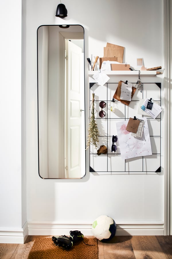 A long LINDBYN mirror, a black steel wire SÖSDALA memo board with clips and a shelf keeping memo notes and sunglasses.