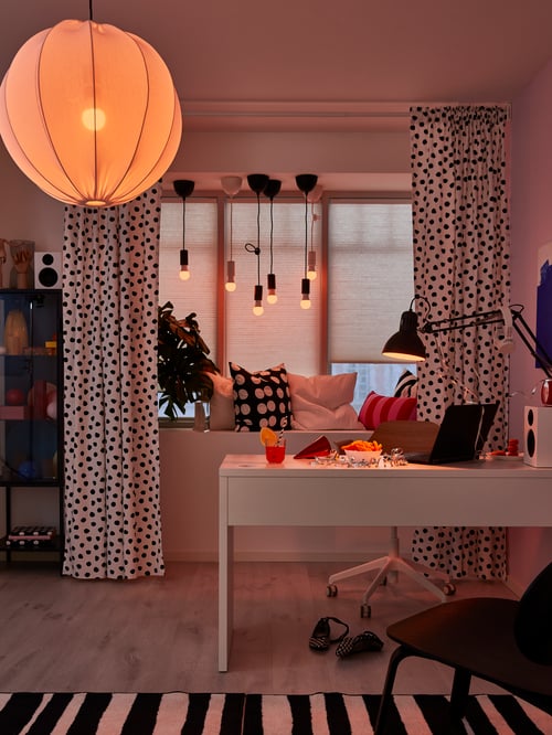 Workspace with a white pendant lamp shade spreading a diffused decorative light, a striped rug low pile and a dotted fabric.