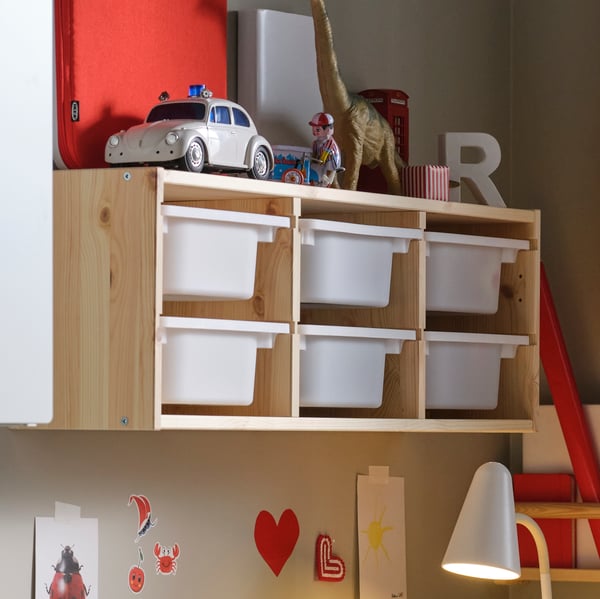 Uno scaffale a parete TROFAST bianco chiaro e tinto di pino. Al suo interno, diversi contenitori e sopra vari oggetti.