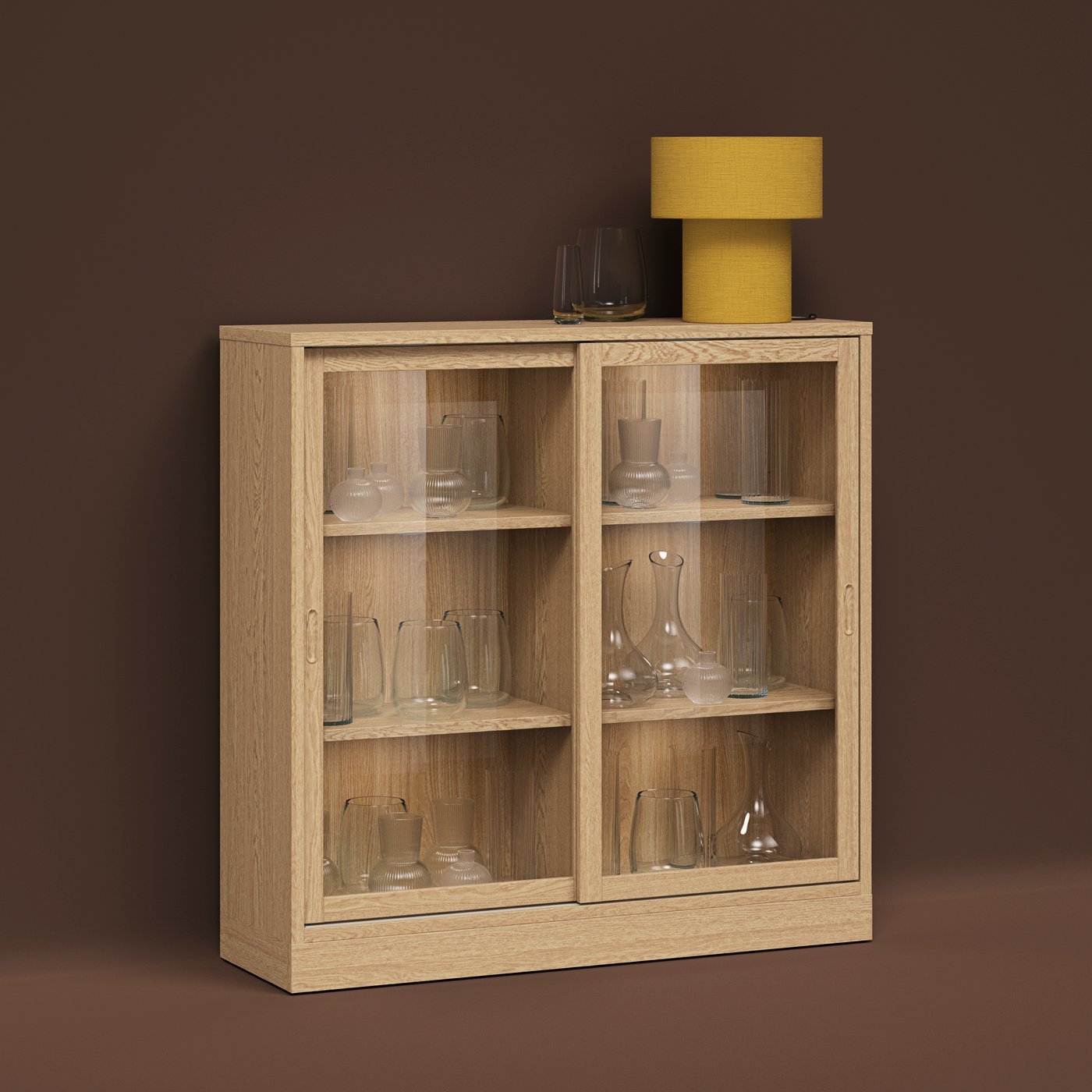 A STOCKHOLM table lamp atop a TONSTAD oak-veneer cabinet holding glassware, all set against a brown background.