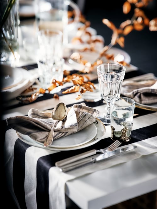 A section of a table decked out for celebration, with white OFTAST plates, POKAL wine glasses, and beige UPPHÖJD cutlery.