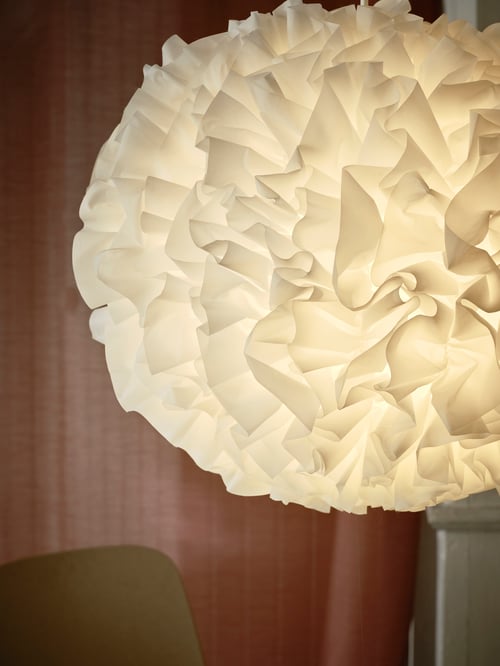 O fotografie de aproape a unei lămpi rotunde cu pandantiv alb atârnând deasupra unui spătar maro închis. Lampa pandantivă este aprinsă.