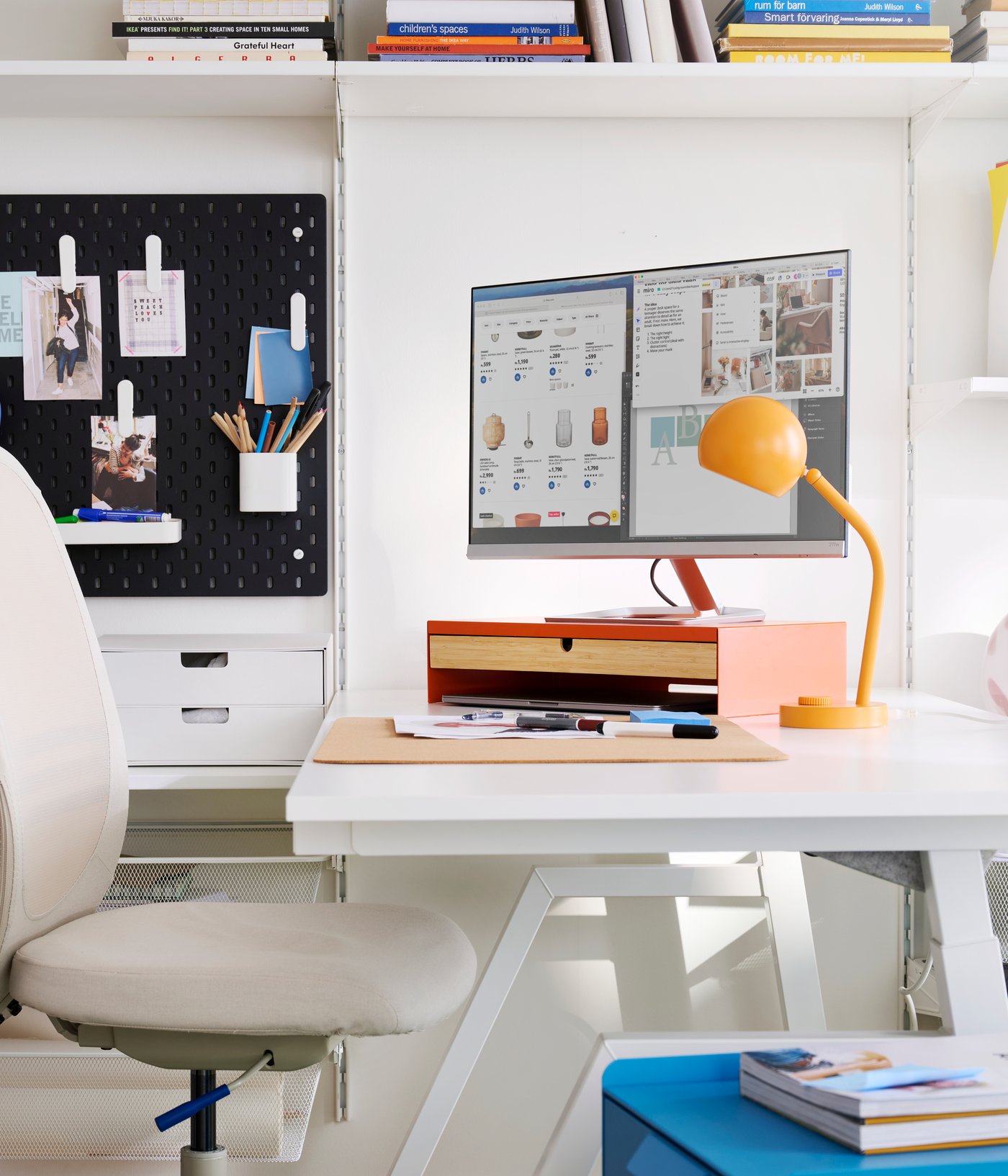 A workspace featuring a bright orange ELLOVEN monitor stand with a drawer on a white desk with a stylish chair.
