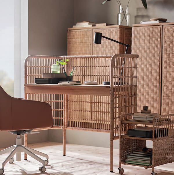 A rattan FRYKSÅS desk in a bright room with a rattan FRYKSÅS storage unit on castors beside it and a work chair in front.