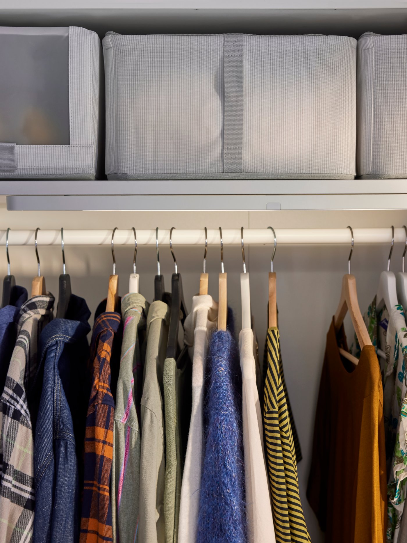 Close-up of PAX wardrobe with hanging clothes and textile storage boxes on shelf above.