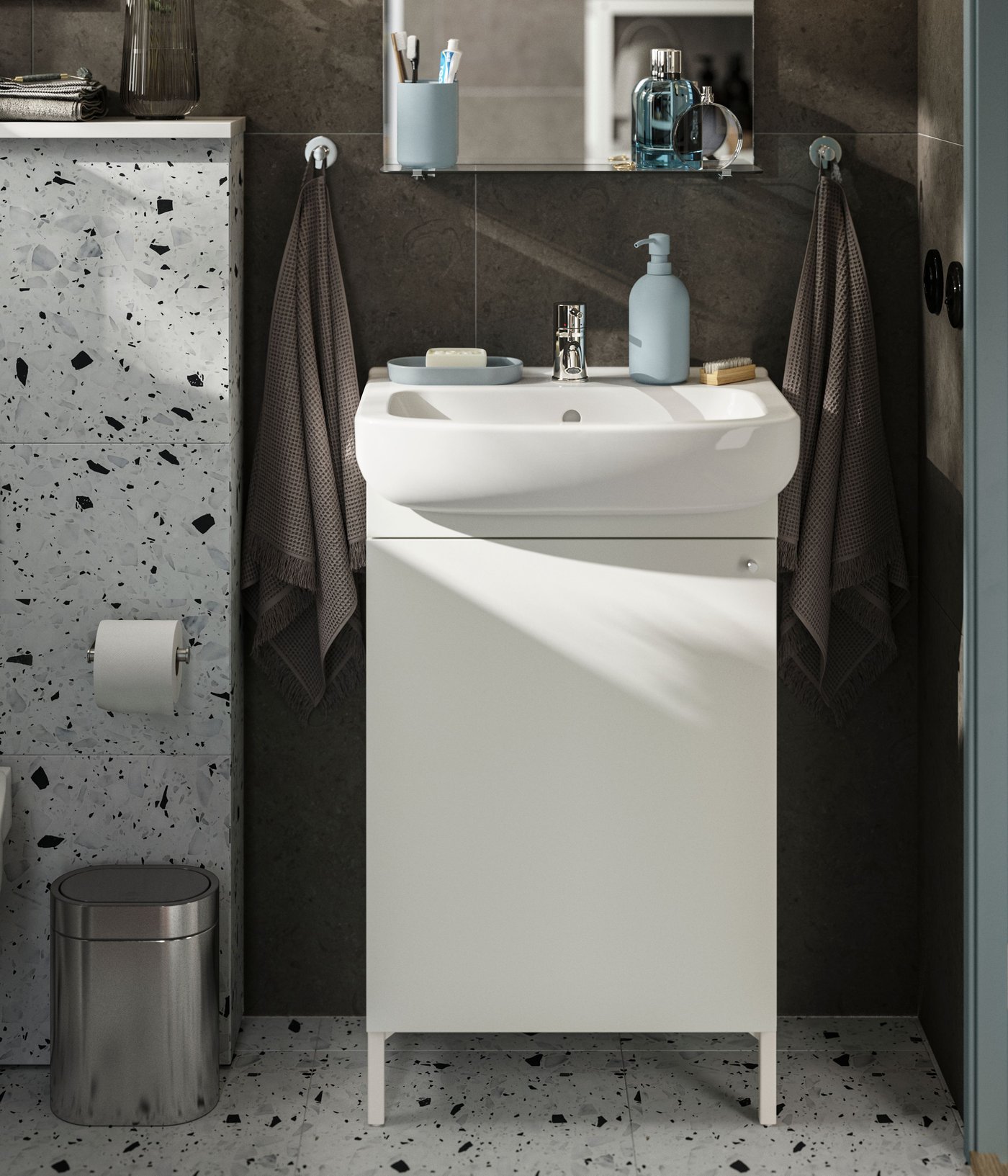 A white NYSJÖN wash-basin cabinet is placed next to a toilet in a bathroom with dark walls and a white floor with dots.