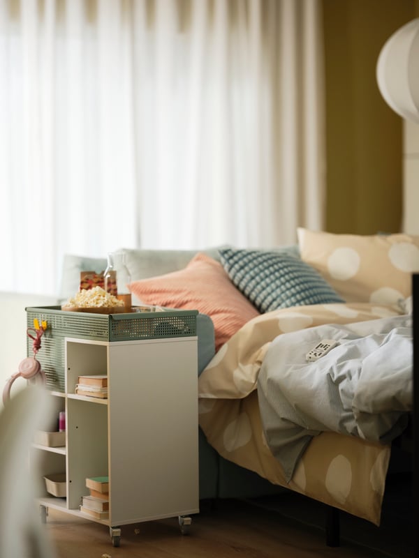 A VIMLE 3-seat sofa bed is made into a bed with cozy bedlinen. An ÖVNING trolley is beside it with popcorn and drinks.
