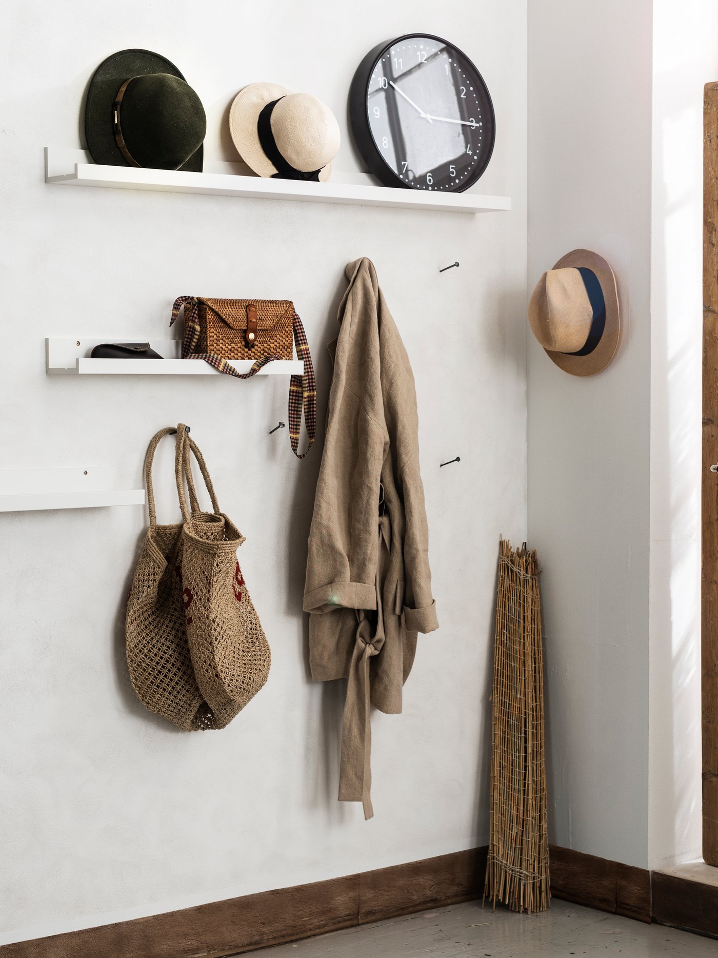 Entrance hall with white walls and two shelves with hats, a bag and accessories. Hooks with hanging basket and clothes, and a wooden door with a hat on the side.

