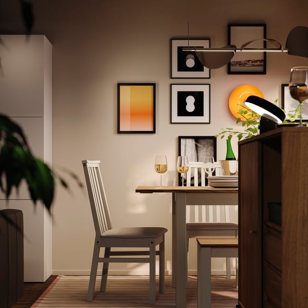 A dining area at night with an ÅLHULT dining set with an extendable table, a bench and chairs and a round, orange LED lamp.