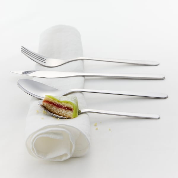 Primer plano de un juego de utensilios FÖRNUFT encima de una servilleta blanca. Hay un trozo de tarta de cumpleaños en la cucharilla.