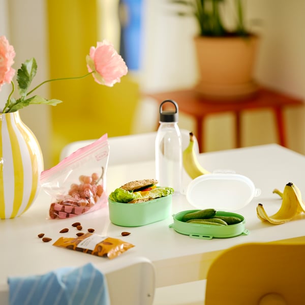 A table with IKEA 365+ water bottle in dark grey, UTBJUDA stackable lunch box in light green and MUNSBIT roasted almonds.