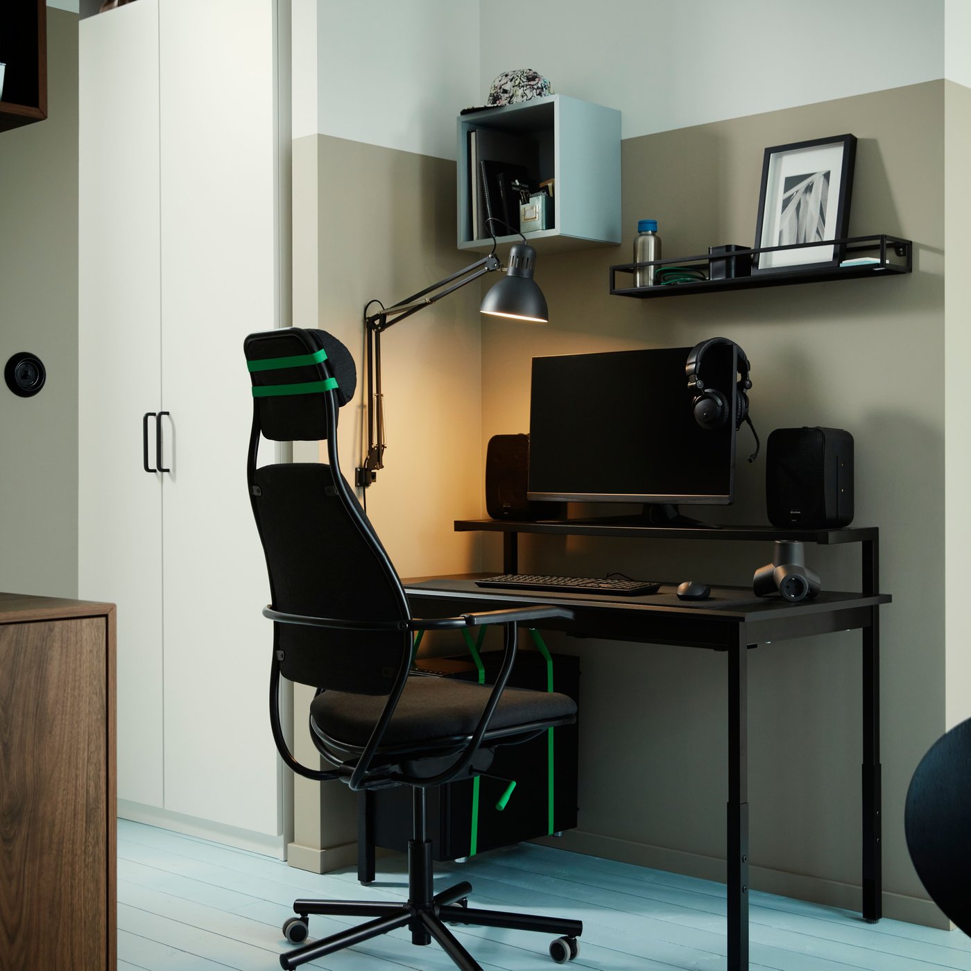 A LÖPARBANA gaming chair stands at an UTVISNING gaming desk with shelf in a corner with some storage mounted on a wall.