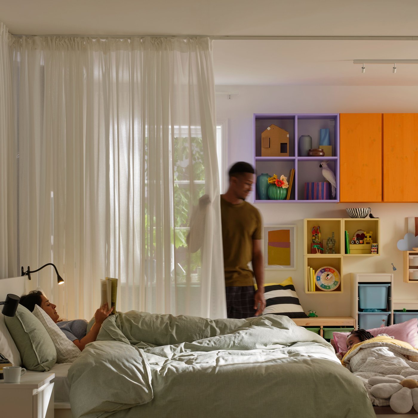 Osoba zaciąga zasłony zawieszone na pojedynczej szynie VIDGA obok łóżka, na którym leży druga osoba.