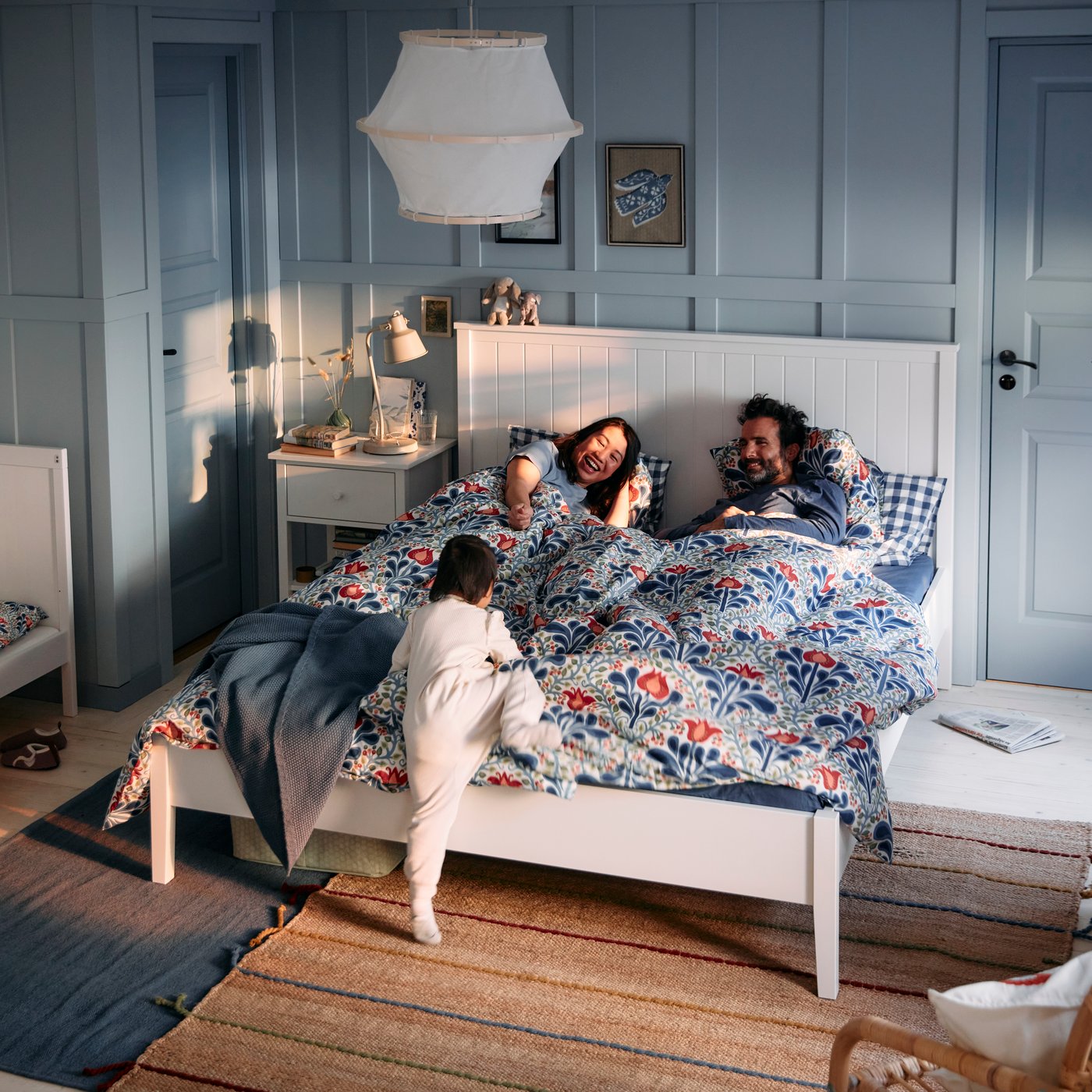 A bedroom with a floral SÄTERVIDE duvet cover on a white bed where two people and a child are playing.