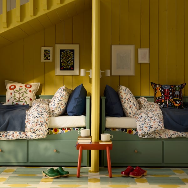 Two grey-green HEMNES day-bed frames with 3 drawers feature duvet covers and cushions against a colourful backdrop.