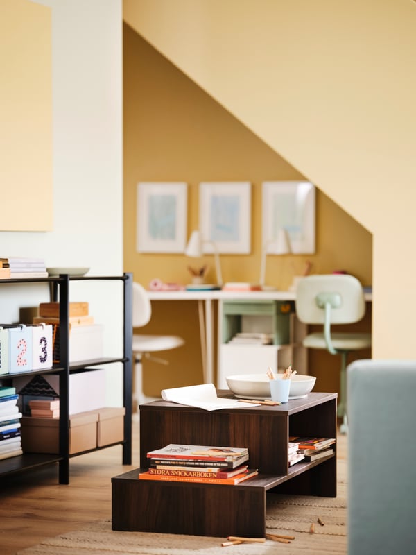 A HOLMERUD coffee table is in the middle of a yellow living room, close by a study nook under the stairs.
