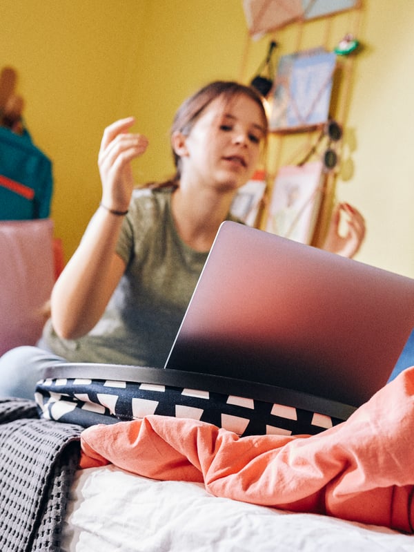 A school child studies on her computer while sat on her bed, the laptop held steady by a BYLLAN laptop support.