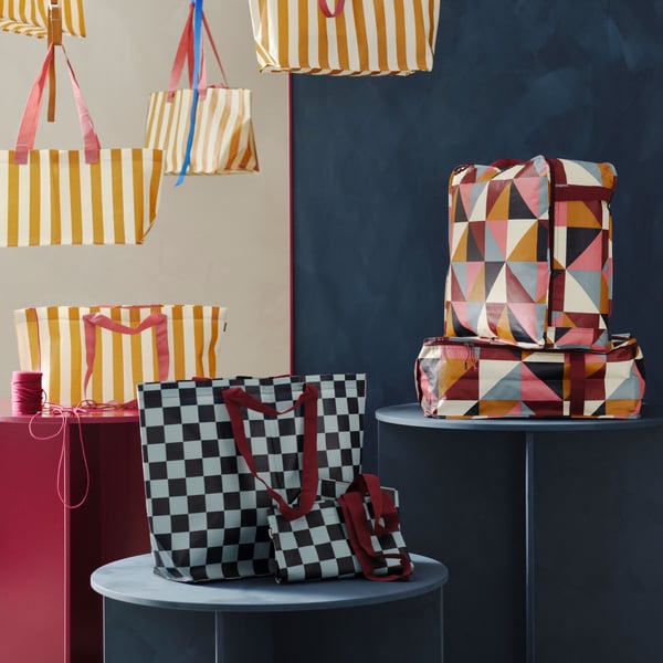 Bolsas de almacenaje y con asas de diferentes estampados pertenecientes al modelo  KLIPPNEJLIKA. A la izquierda bolsas de rayas verticales amarillas y blancas, en el centro dos bolsas de cuadrados en diferentes tonos de azul y a la derecha cajas de estampado geométrico en tonos granate, naranja, beige y azul apagados. 