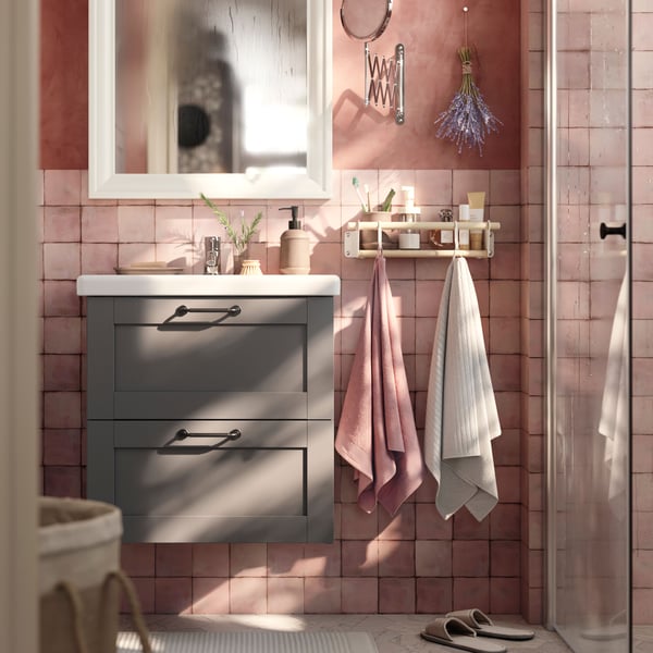 A grey HAVBÄCK wash-stand with drawers and a mirror cabinet are placed in a bathroom with soft pink walls and a grey floor.