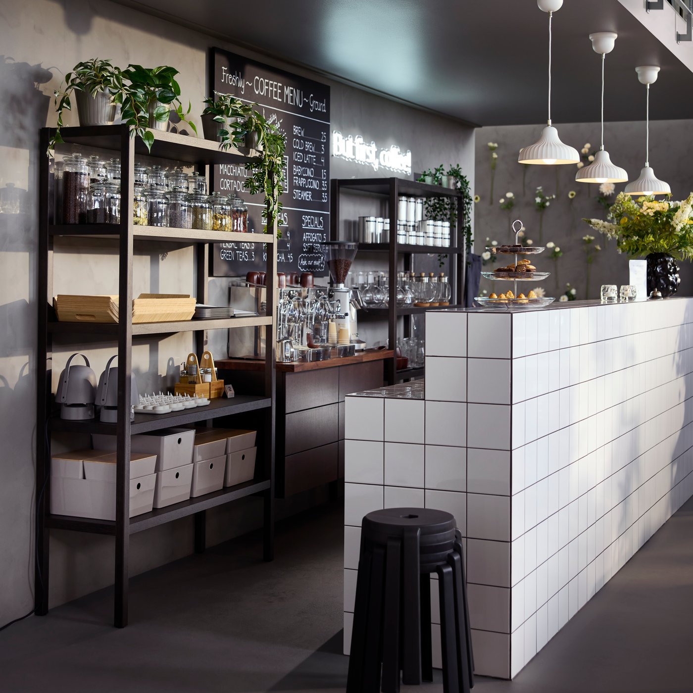 A café counter with dark brown STOCKHOLM 2025 shelving units in oak veneer/dark brown filled with glassware and jars.