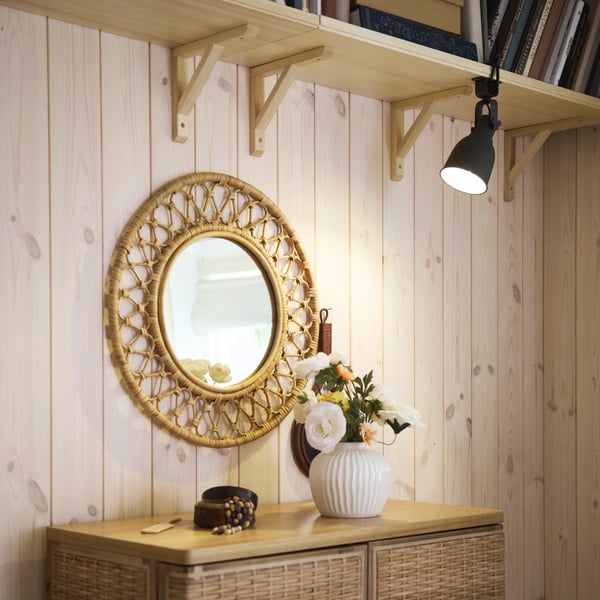 A HEKTAR wall/clamp spotlight attached to a shelf lights up flowers in a white PELARBJÖRK vase in front of a GRINSBOL mirror.
