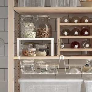 A pantry has IVAR shelves with PÅLYCKE clip-on baskets and VARIERA insert shelves and bottles and jars are stored there.