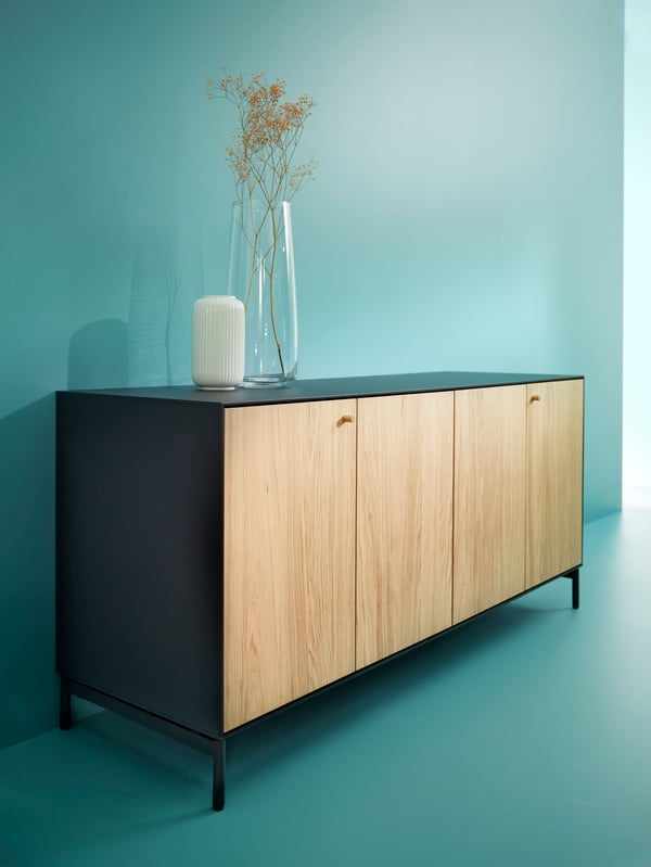 A teal-coloured room with a BOASTAD sideboard in black/oak veneer placed against a wall. There are two vases on top.