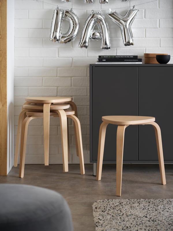 Four KYRRE stools in birch next to a dark-grey EKET cabinet with doors, in front of a white wall in a living room.