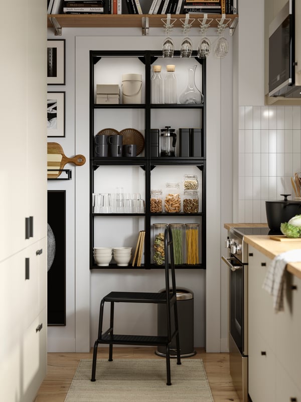 A parallel kitchen with beige HAVSTORP fronts has an ENHET wall frame with shelves in anthracite and a BÄSINGEN step stool.