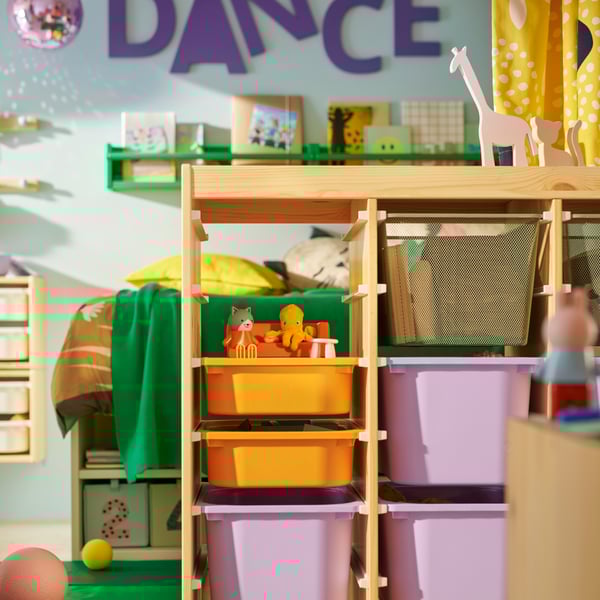 A TROFAST room divider in the middle of a shared chidren’s bedroom with orange, lilac and mesh boxes in it and toys on top.