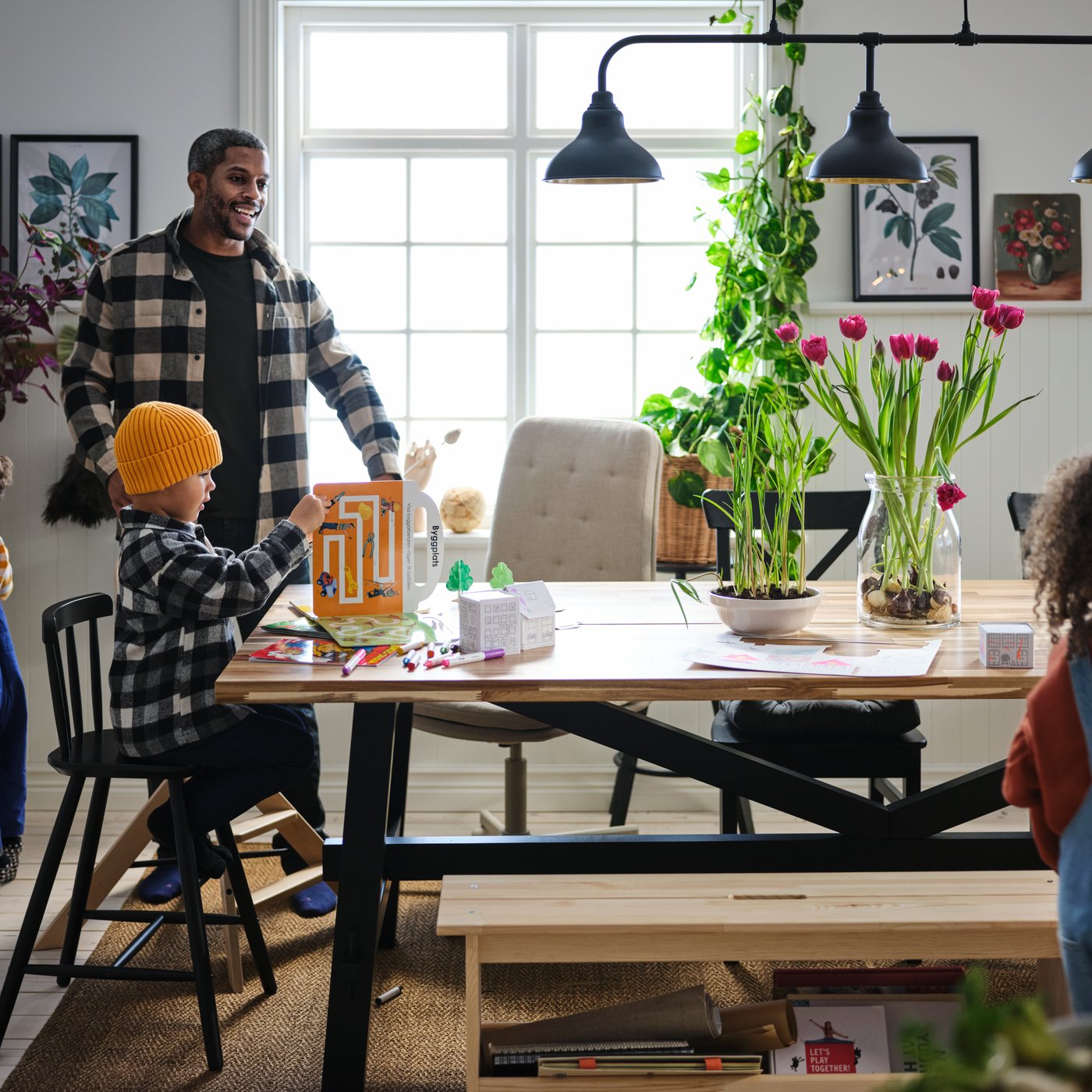 Ein Mann steht lächelnd vor einem SKOGSTA Esstisch an dem zwei Kinder sitzen. Ein Kleinkind steht vor einer HAUGA Anrichte.