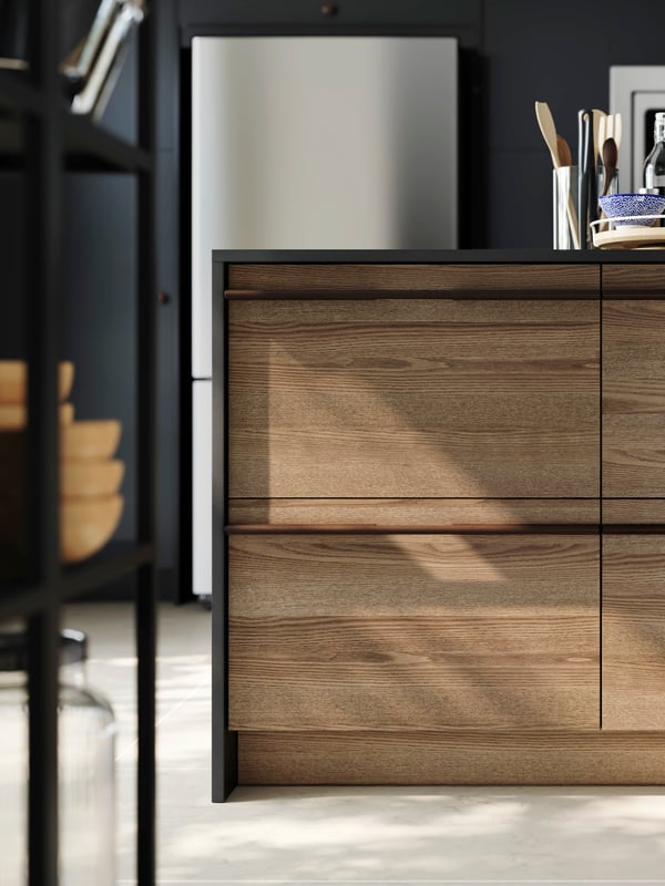 A modern kitchen with STENSTA dark brown ash veneer drawer fronts, a black countertop and a stainless steel fridge.